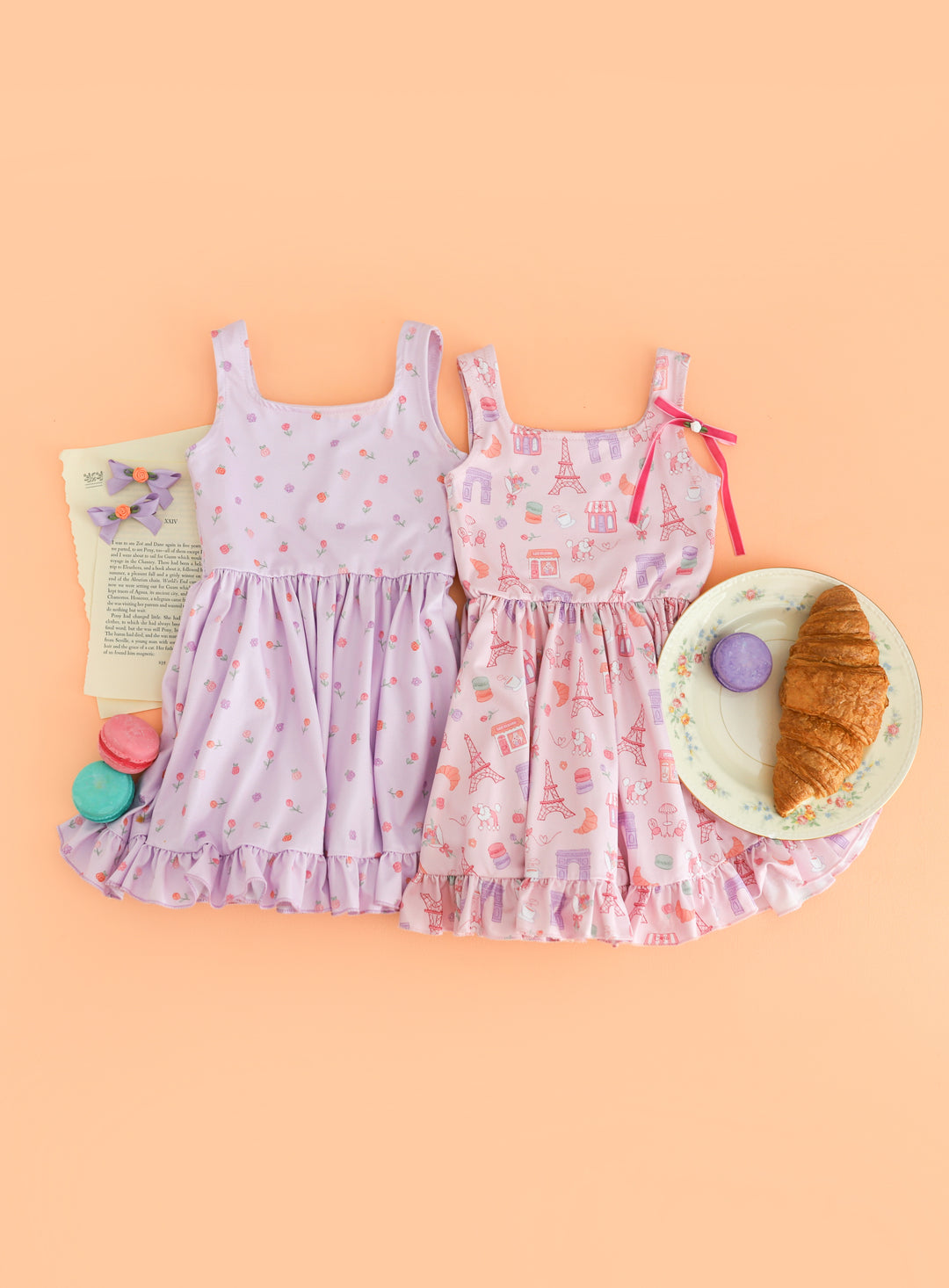 flat lay of two Paris inspired summer twirl dresses styled with rosette bows, macaroons and croissants 