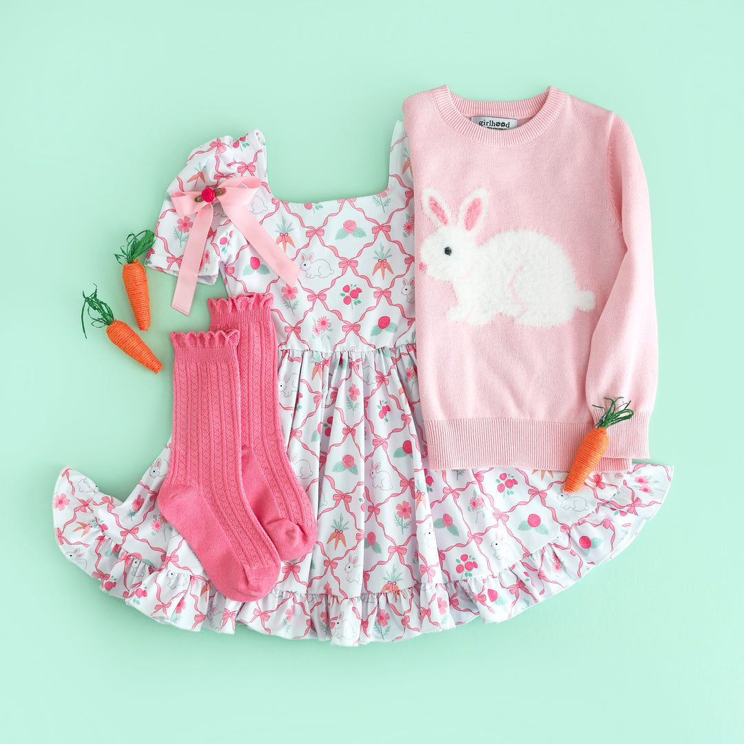 flat lay of girl's easter bunny themed outfit with pink fluffy bunny sweater, white with pink ribbon and bunny print twirl dress and matching socks and bow
