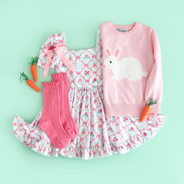 flat lay of girl's easter bunny themed outfit with pink fluffy bunny sweater, white with pink ribbon and bunny print twirl dress and matching socks and bow