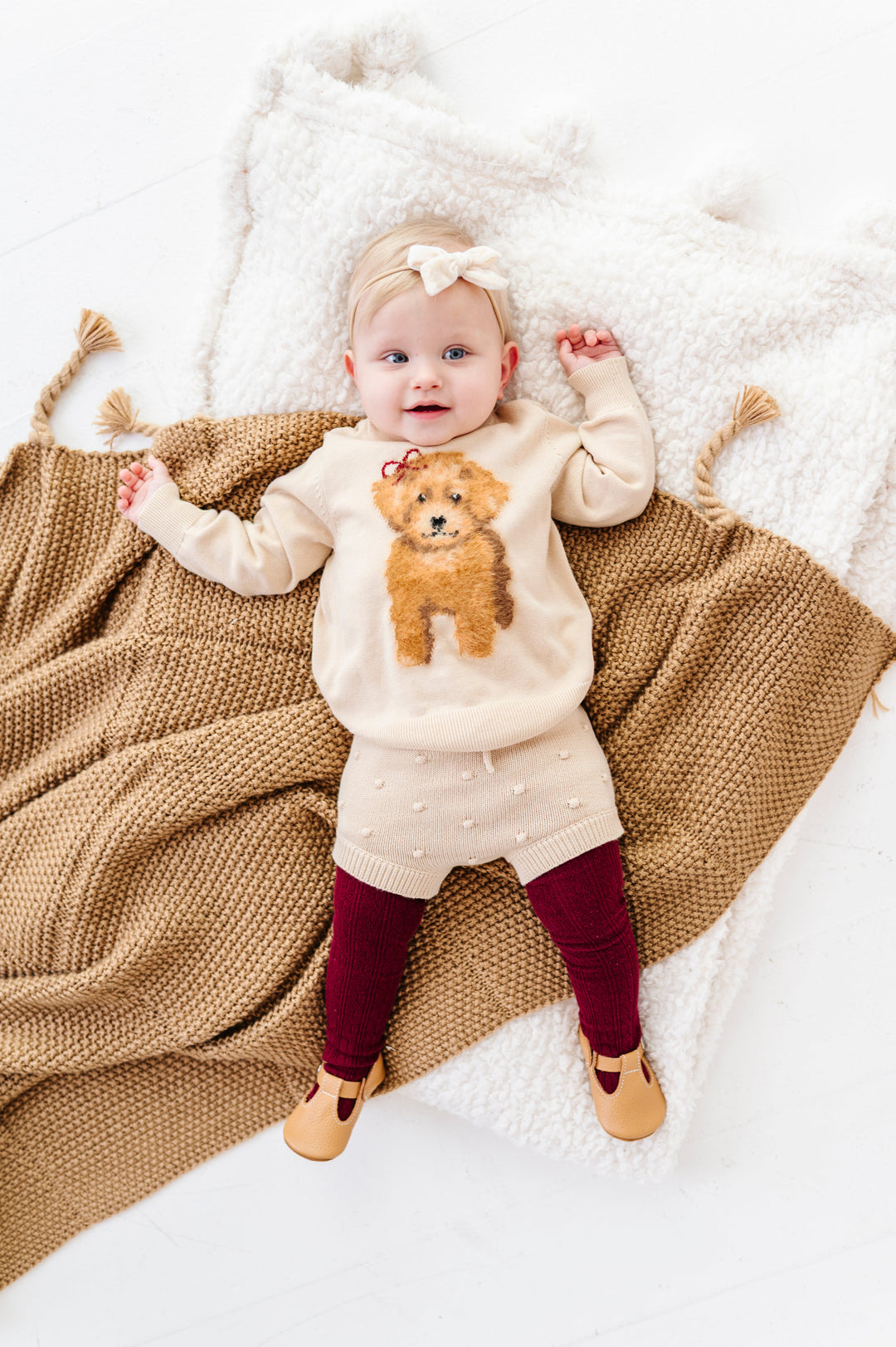baby girl in cream pullover sweater with fluffy yarn puppy design paired with cream bubble knit bloomers, cream velvet baby bow and burgundy cable knit tights