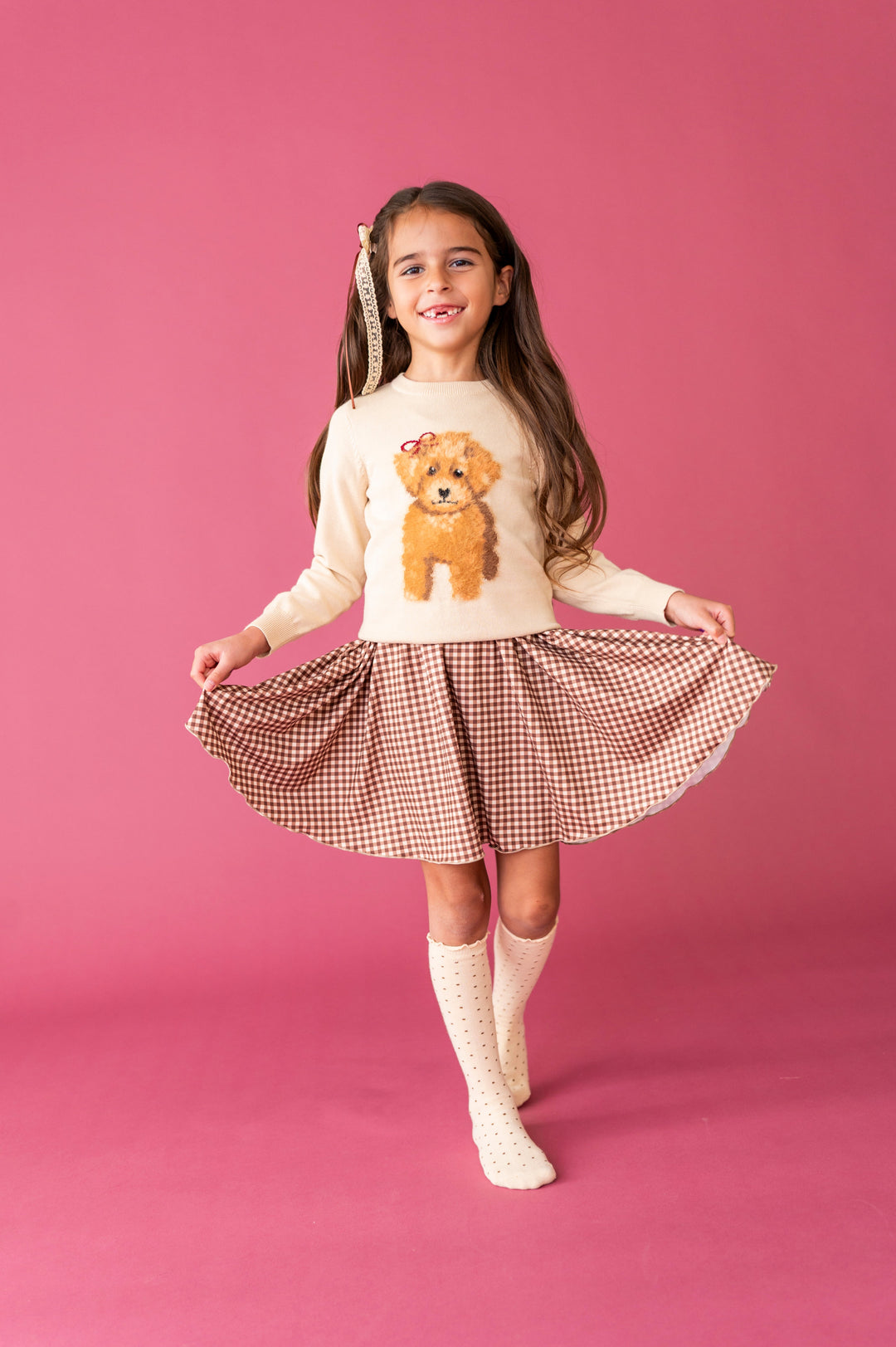 young girl in cream fluffy puppy sweater layered over brown gingham twirl dress with matching cream dotted knee socks and lace bow