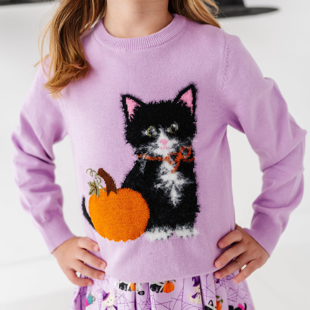 little girl in lavender cotton knit sweater with fluffy black cat next to sparkle yarn pumpkin layered over matching lavender Halloween kitten print dress