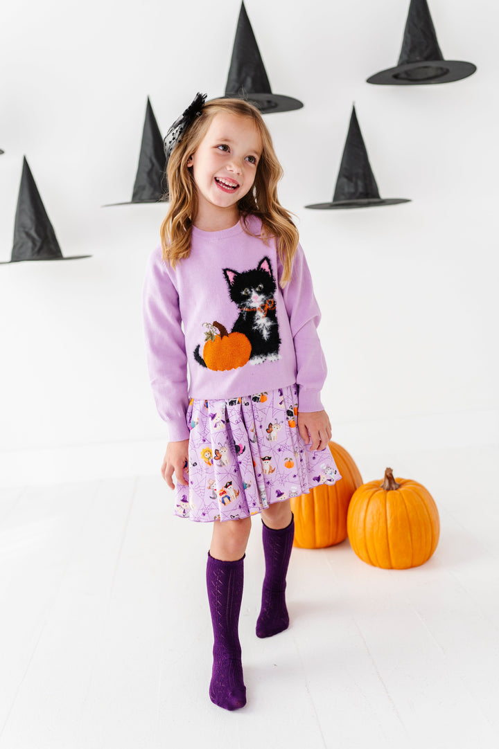young girl surrounded by pumpkins and floating witch hats wearing lavender twirl dress with kittens dressed in Halloween costumes paired with matching purple fluffy kitten and pumpkin sweater, purple pointelle knee socks and sheer black star bow