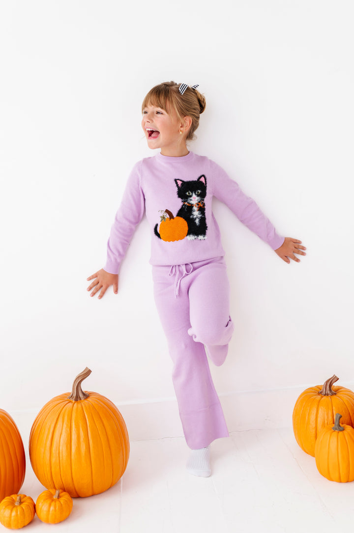 young girl standing by pumpkins in lavender cotton knit sweater with fluffy kitten and sparkly pumpkin paired with lavender sweater pants