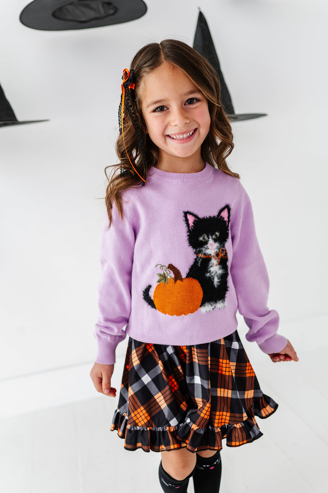 young girl wearing black and orange plaid twirl dress paired with lavender fluffy black cat sweater for Halloween