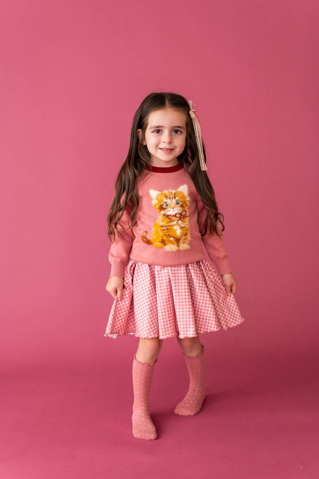young girl in mauve sweater with fluffy yarn kitten design paired with pink gingham twirl dress and matching pink dottie knee socks