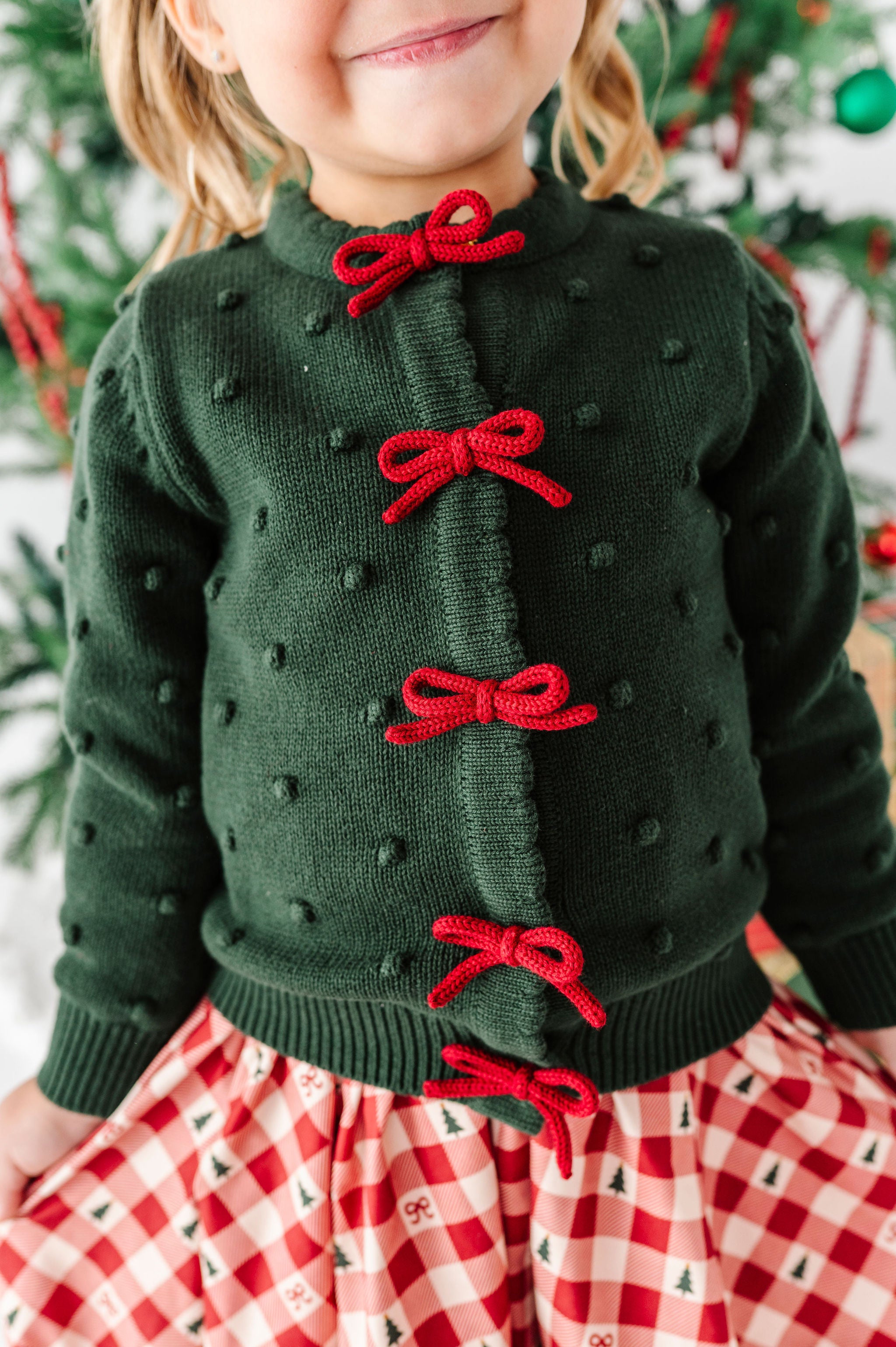 little girl wearing a dark green bubble knit cardigan with crimson red bow design down the placket