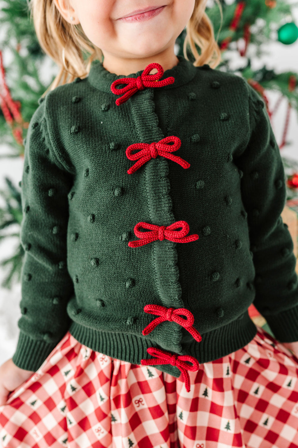 little girl wearing a dark green bubble knit cardigan with crimson red bow design down the placket