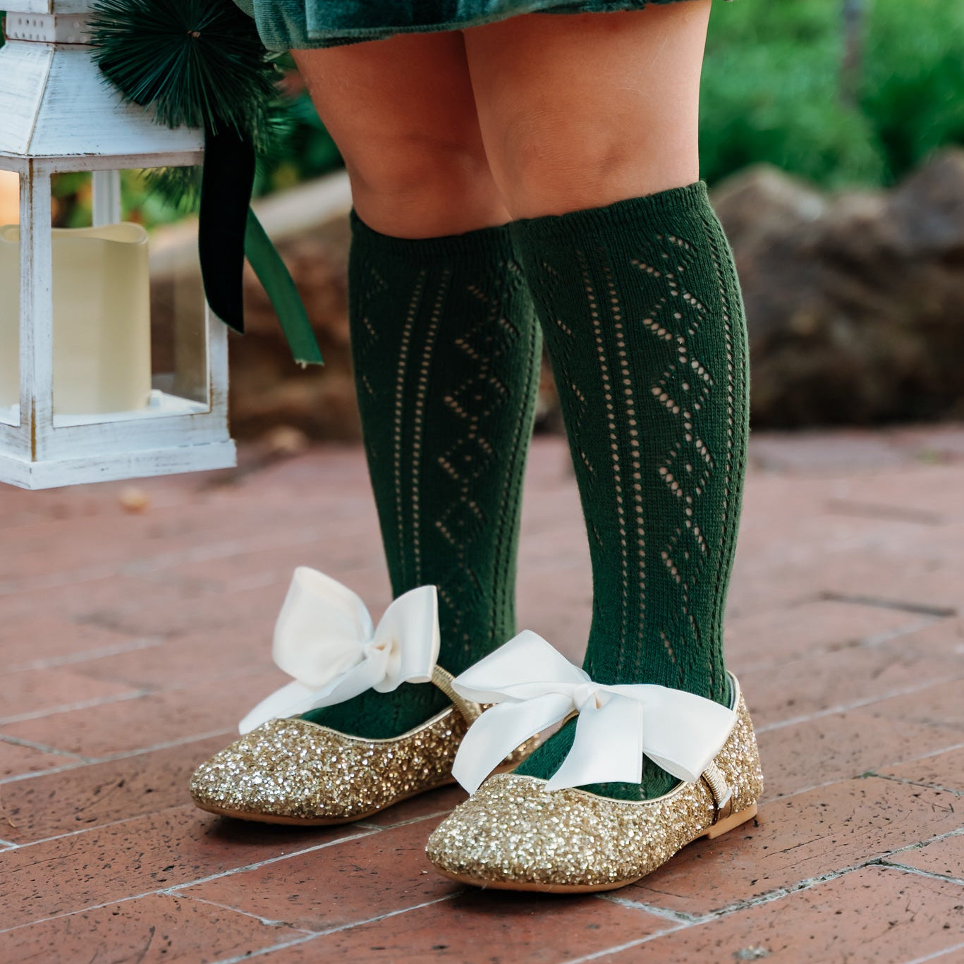 Girl wearing forest green pointelle knit socks gold glitter shoes with ivory bow ties