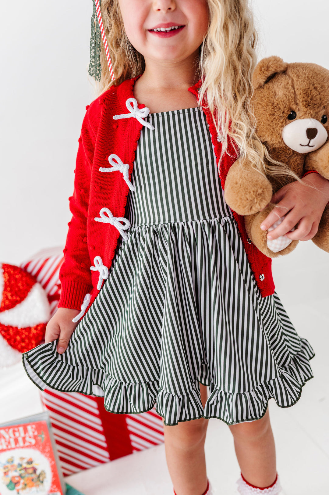 little girl wearing christmas themed outfit with forest green pinstripe dress and red sweater with white bows