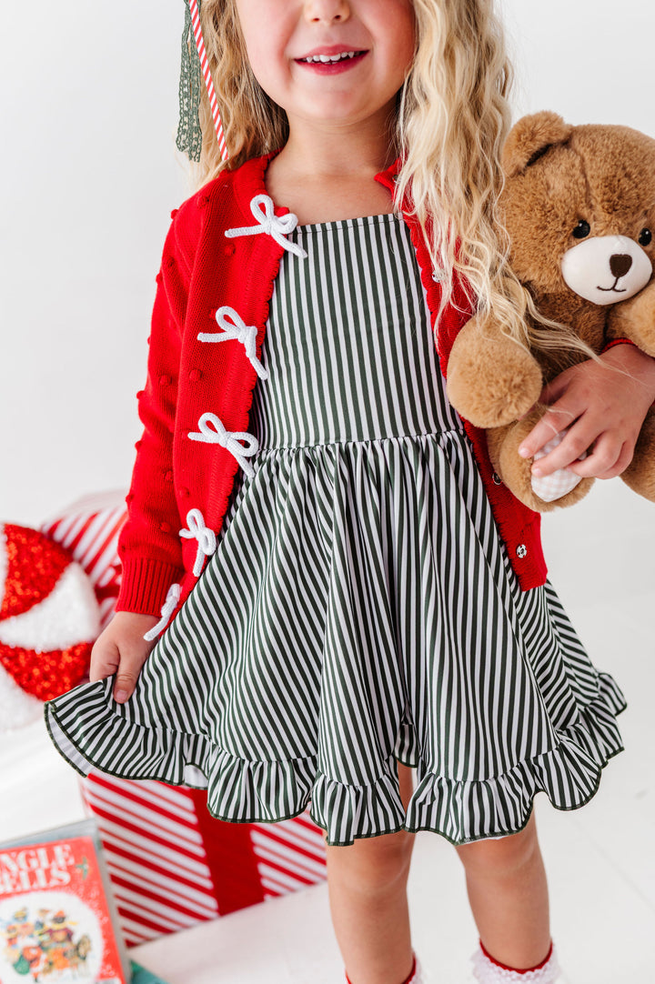little girl wearing christmas themed outfit with forest green pinstripe dress and red sweater with white bows