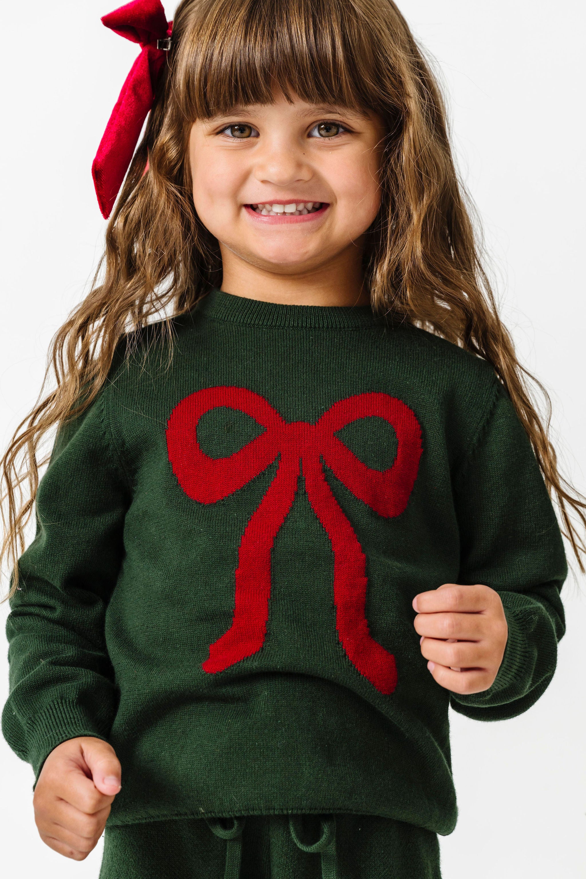little girl in forest green knit sweater with red bow design and matching green sweater pants