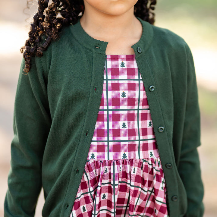 little girl in red gingham and green pine tree print Christmas dress and matching forest green knit cardigan with buttons