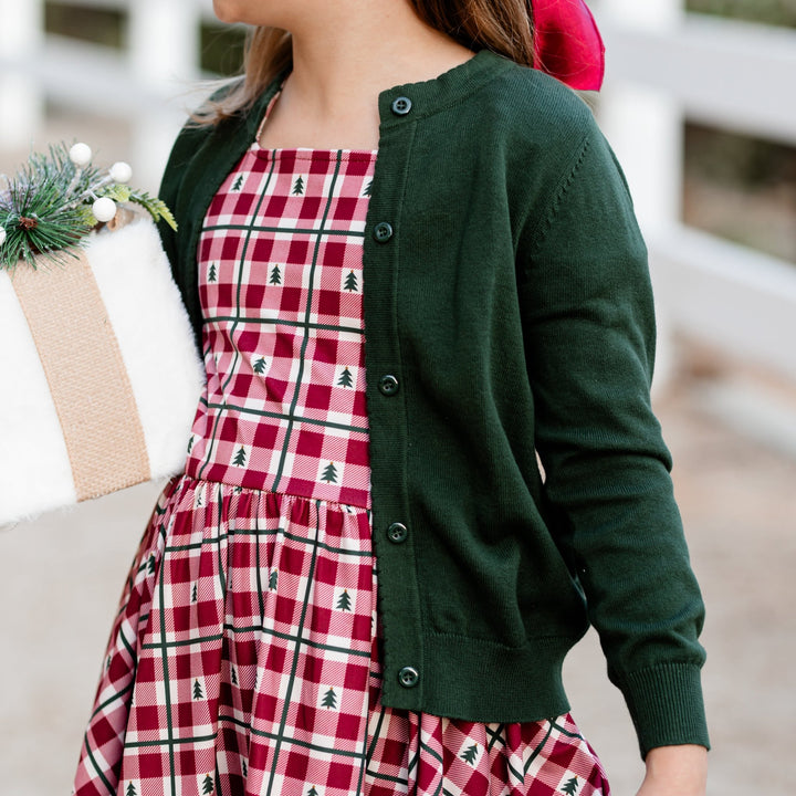 little girl holding Christmas gift in forest green cardigan with matching crimson tree dress 