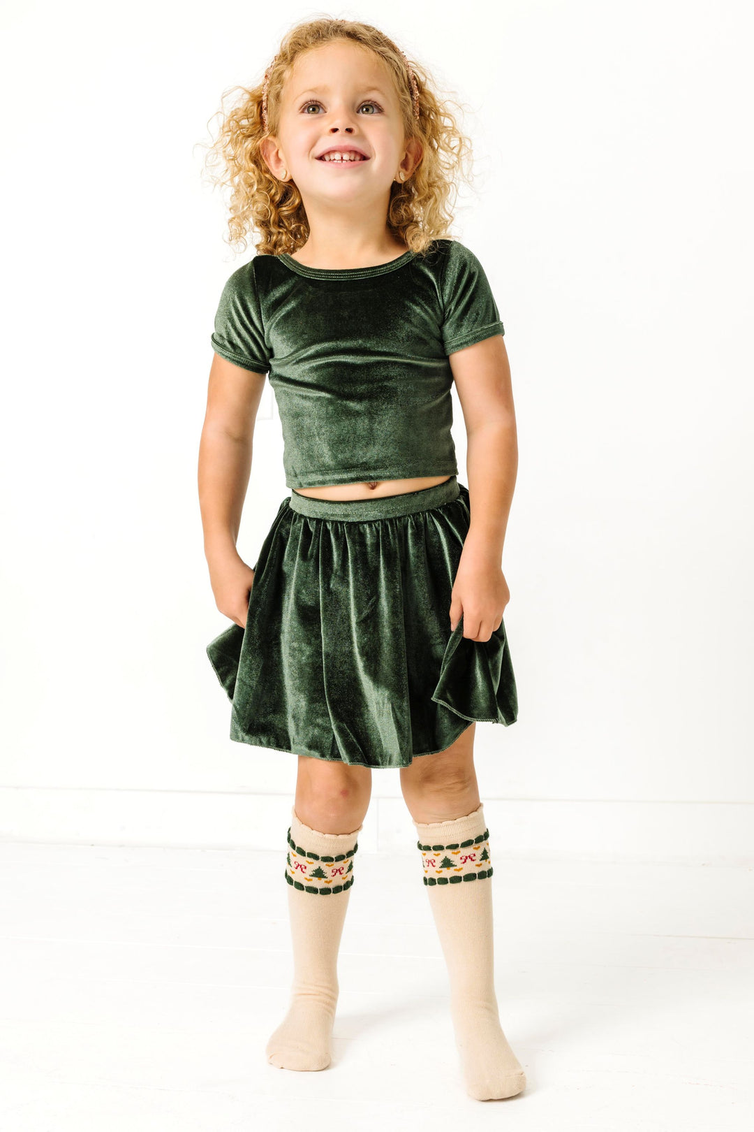 little girl in matching forest green velvet top and skirt paired with cream knee highs with Christmas fair isle print and scalloped trim