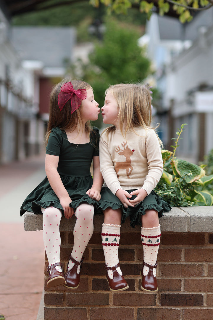 two little girls wearing matching dark green dresses with christmas accessories