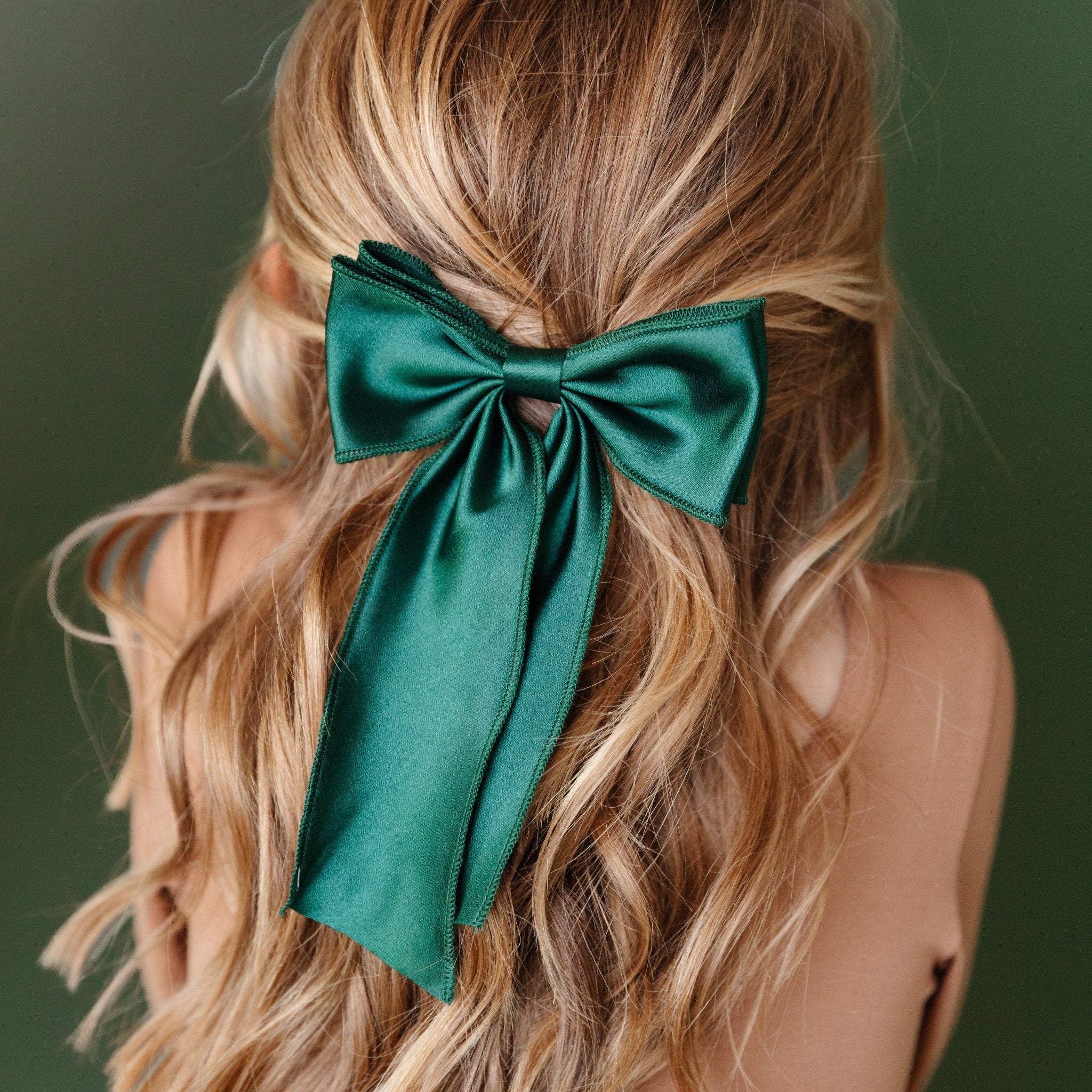 little girl in neutral colored dress with large satin green bow for Christmas