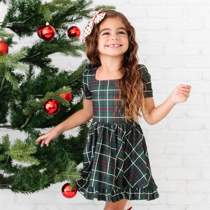 girl wearing forest green plaid christmas dress with matching knee high socks and hair bow