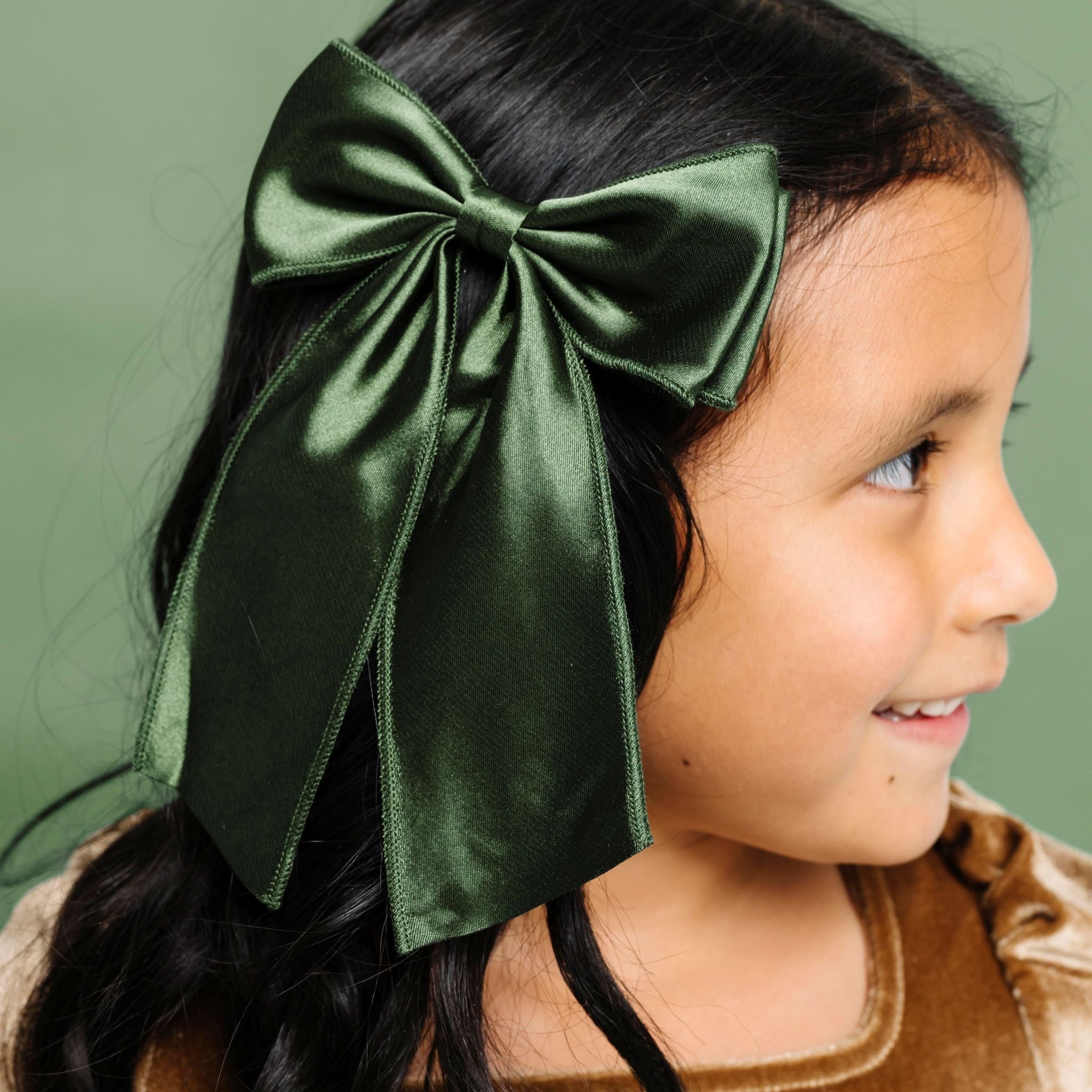 young girl in deep green satin double bow on clip paired with gold velvet Christmas dress