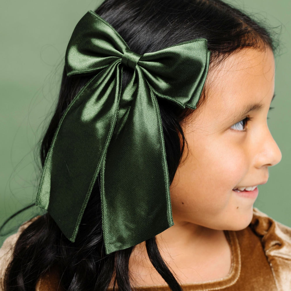 young girl in deep green satin double bow on clip paired with gold velvet Christmas dress