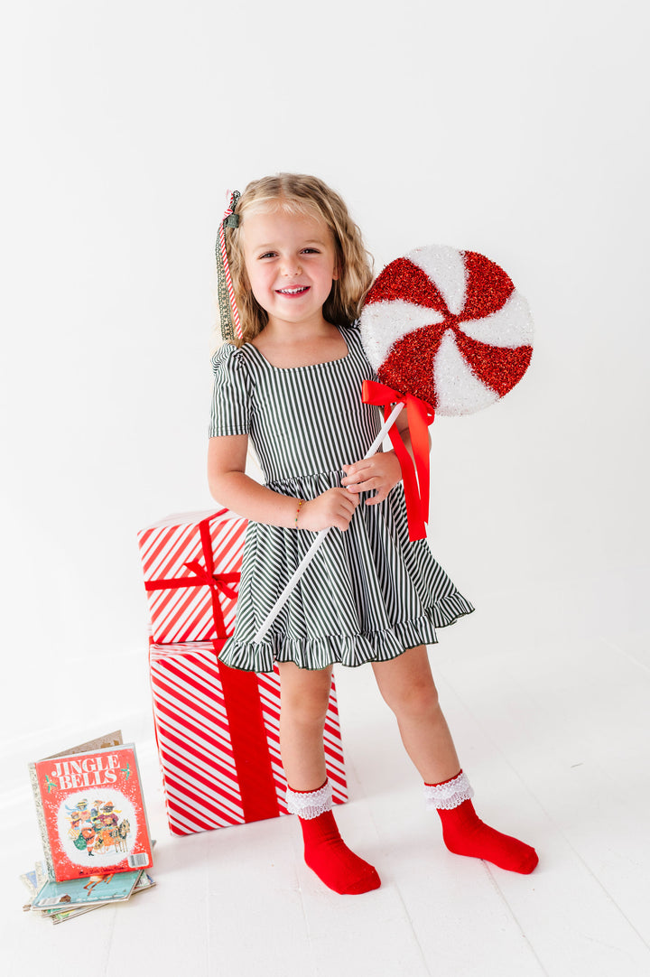 little girl wearing green and white stripe christmas dress holding christmas lollipop