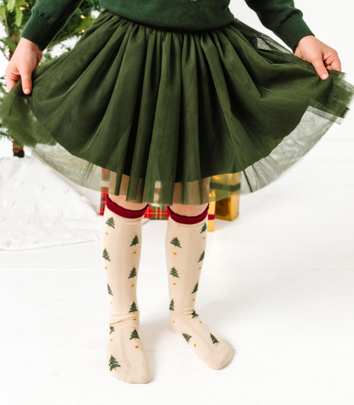 girl in forest green tulle skirt with coordinating cream knee high socks with crimson scalloped trim and Christmas tree print 