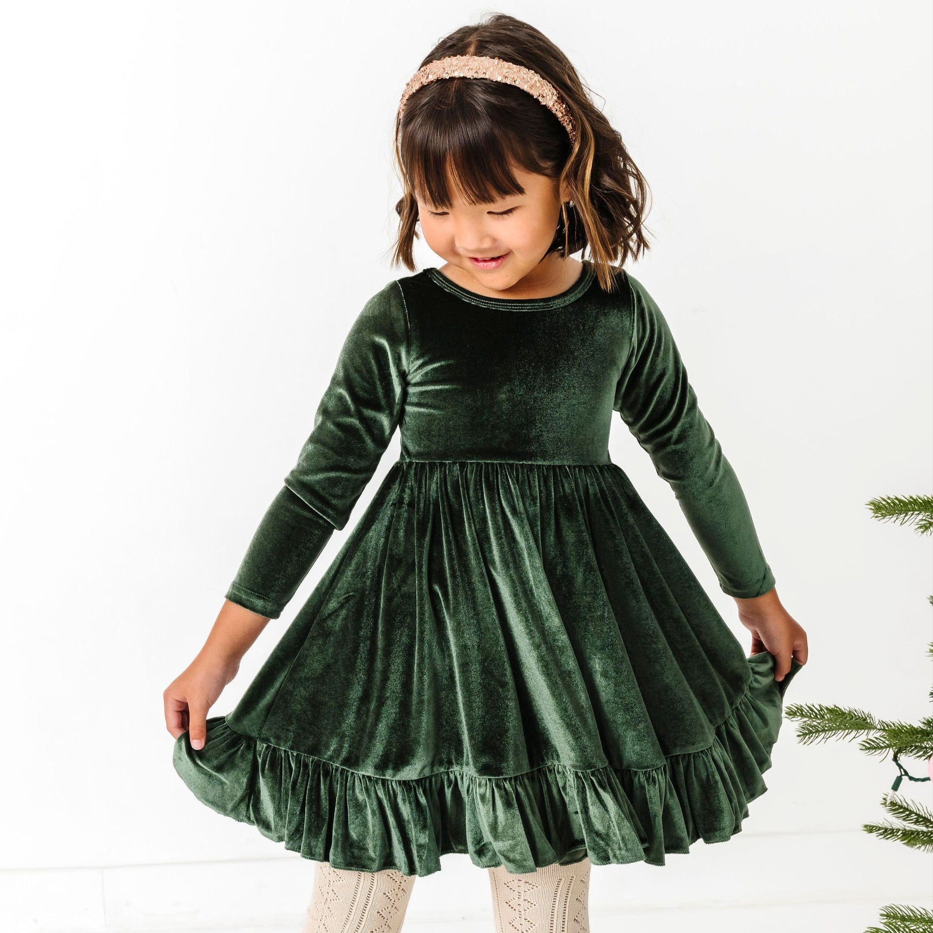 little girl in forest green long sleeve twirl dress paired with cream open knit tights and sparkly gold headband for winter