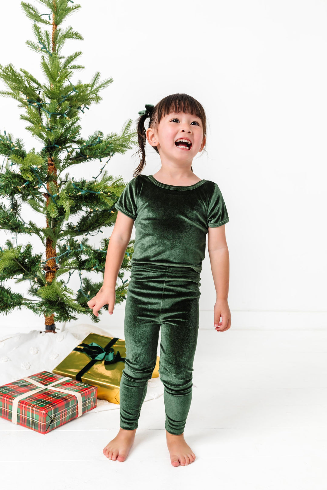 little girl in matching forest green velvet top and leggings by Christmas tree