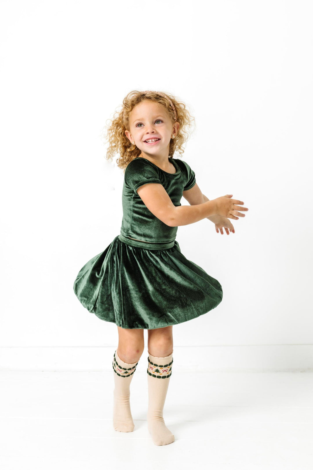 little girl twirling in forest green velvet top and skirt with fair isle print holiday knee highs for Christmas