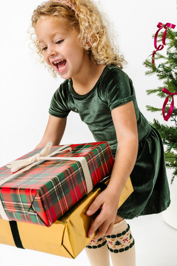 little girl holding Christmas gift in forest green velvet top and matching skirt