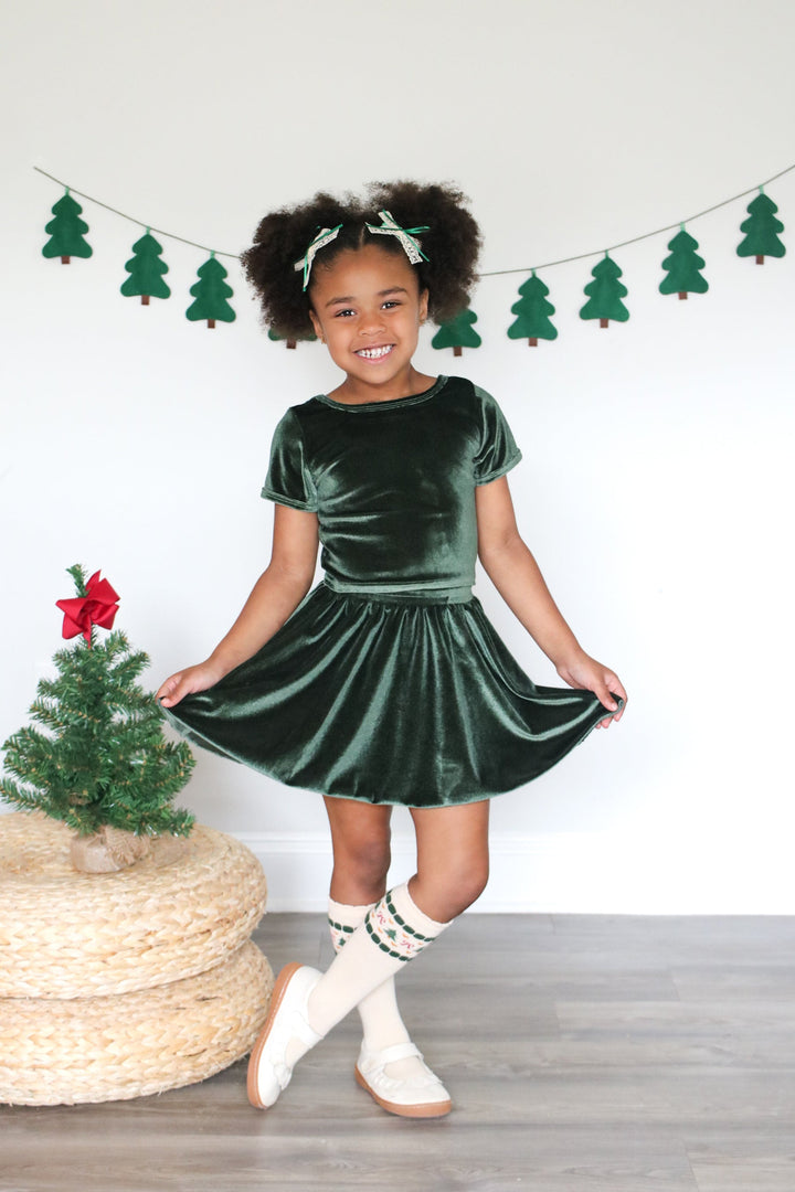 young girl in forest green velvet fitted top, matching skirt and cream knee-high socks with fair isle Christmas design