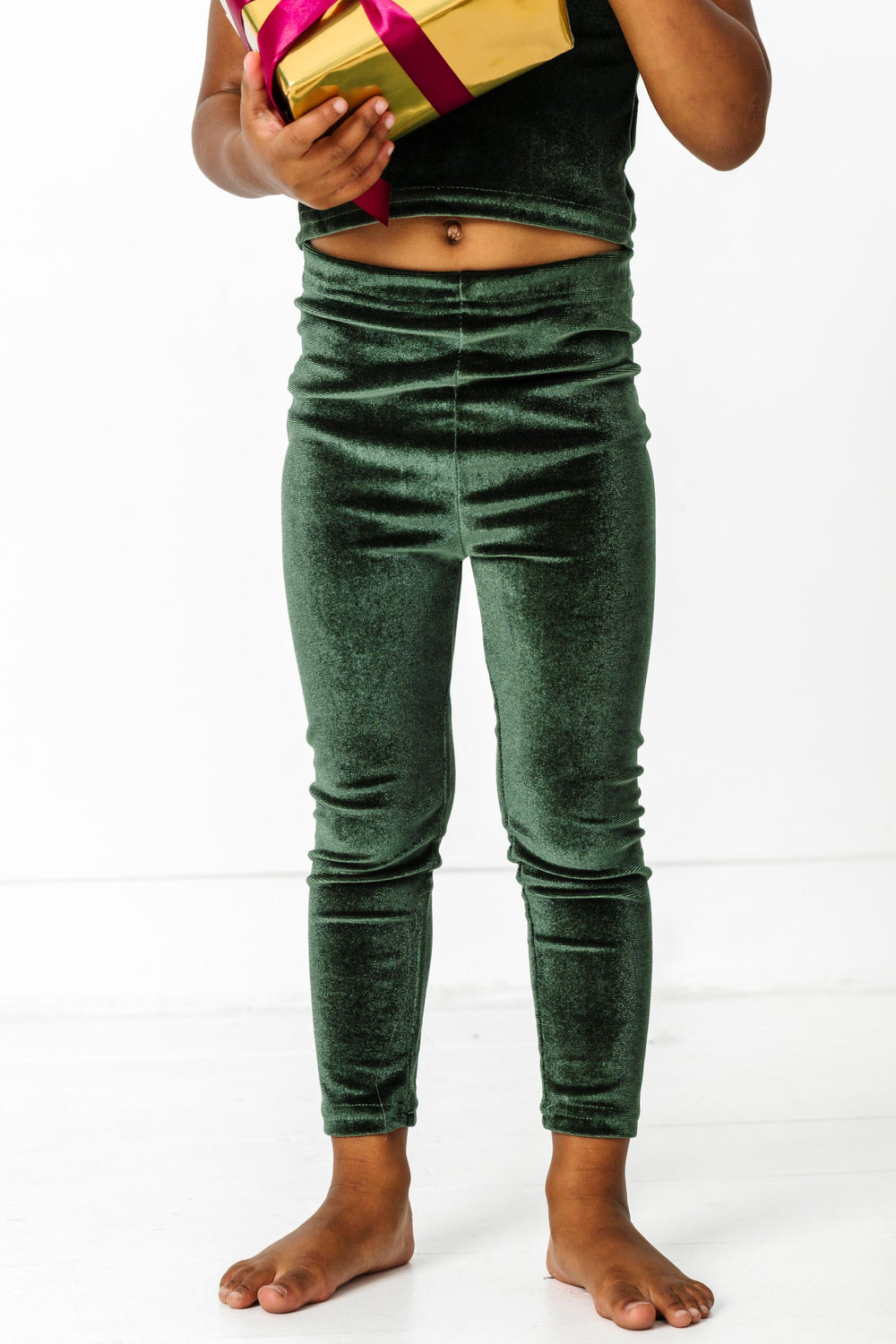 little girl holding Christmas gift in forest green velvet leggings and matching top