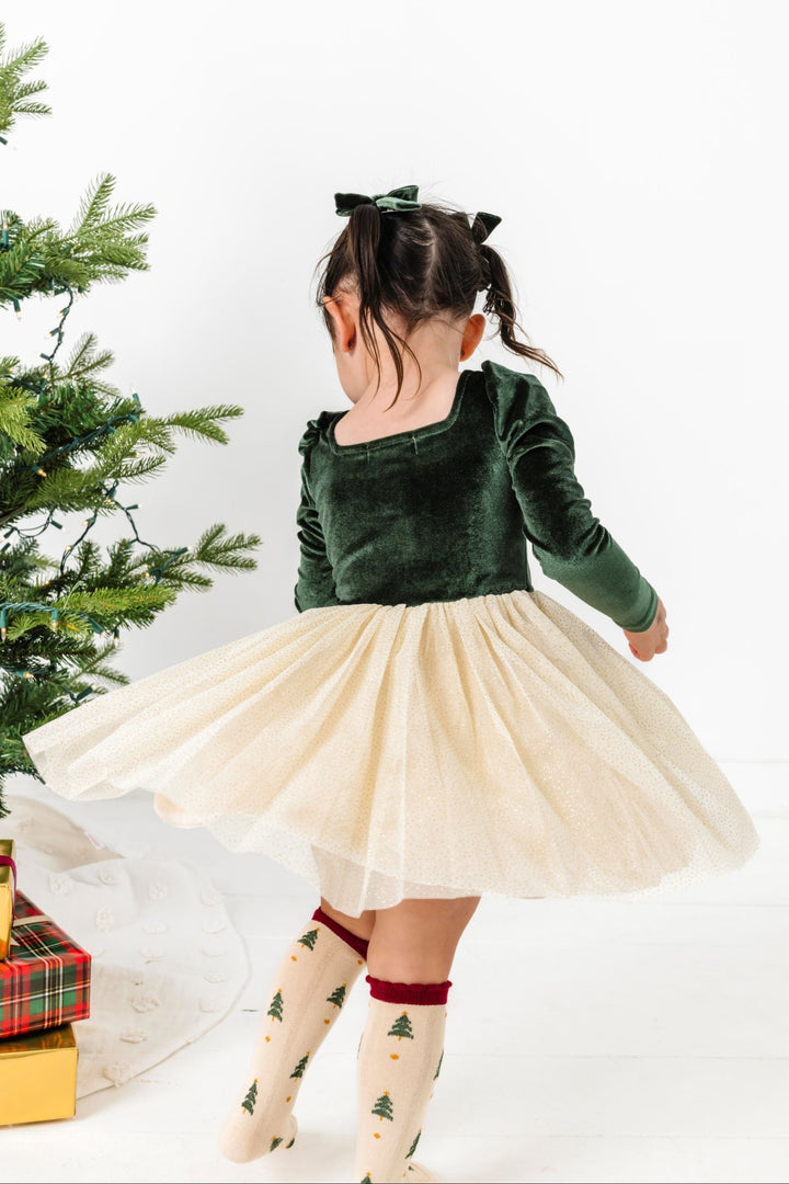 little girl twirling in long sleeve tutu dress with forest green velvet bodice and cream sparkle tulle skirt paired with cream knee high socks with crimson scalloped trim and Christmas tree print
