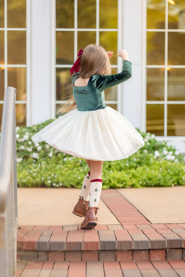young girl twirling in forest green velvet dress with cream sparkly tulle skirt and christmas tree print knee high socks