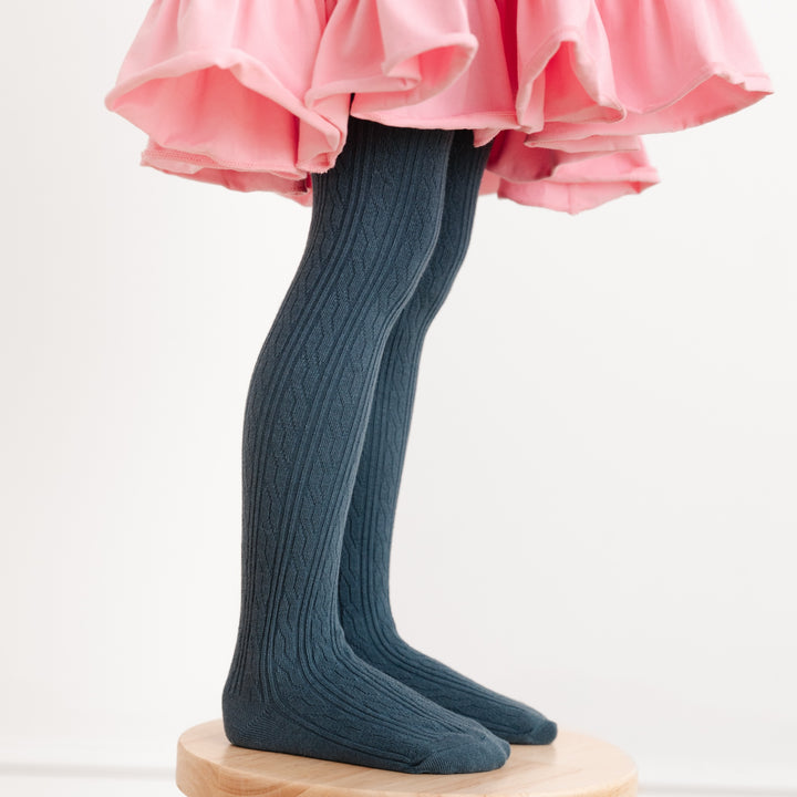 little girl in pink dress standing on wooden stool wearing dark french blue cable knit tights