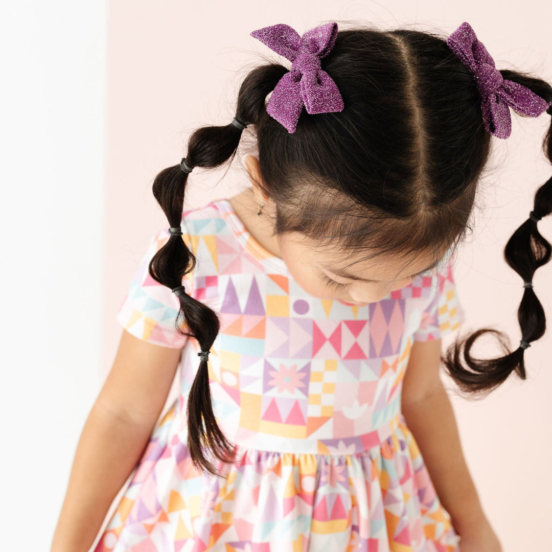 little girl wearing sparkly purple pigtail bows matching her small world inspired dress