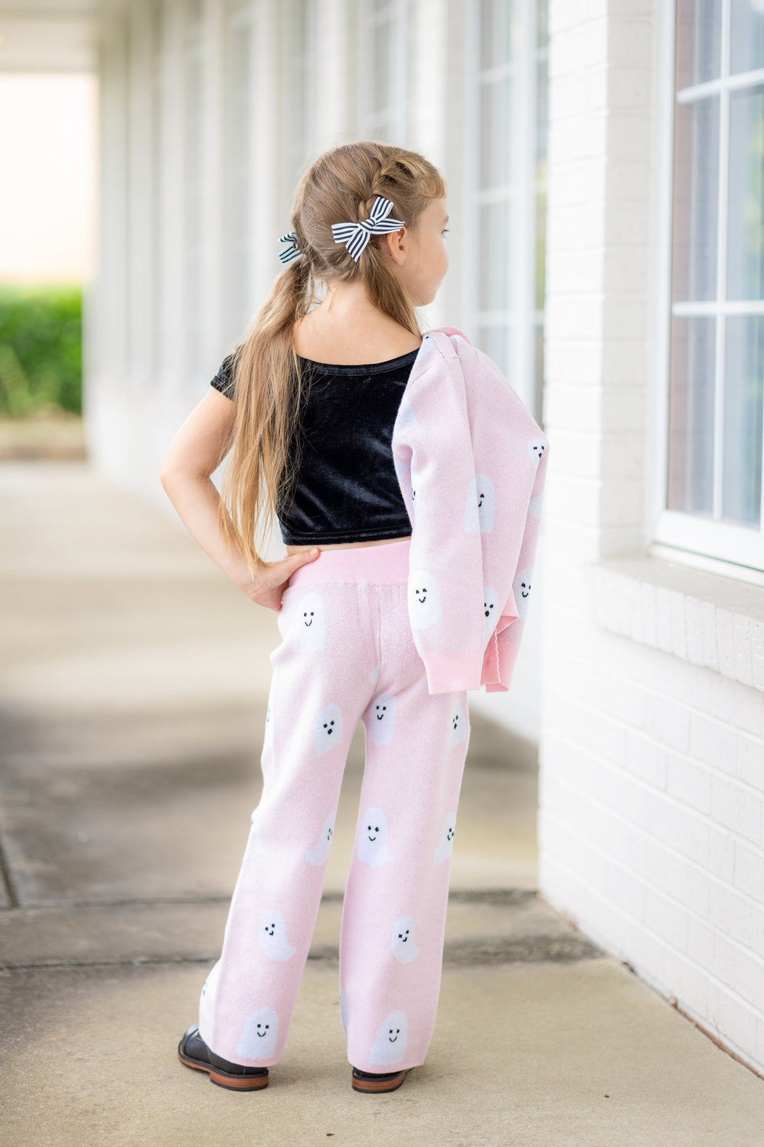 little girl in light pink wearing ghost print sweater pants holding matching cardigan sweater with short sleeve black velvet top and black and white striped pigtail bows 