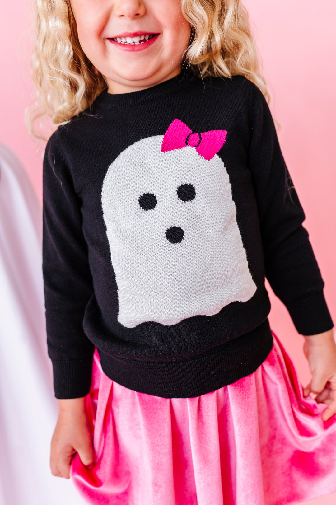 close up of little girl in black knit sweater with white ghost wearing pink bow design on the front paired with pink velvet skort for Halloween
