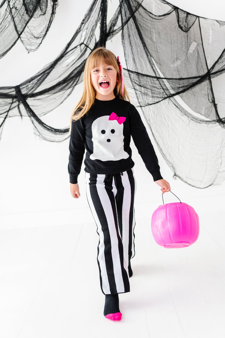 young girl holding pink pumpkin bucket in black and white striped sweater pants paired with white ghost design on black cotton knit sweater