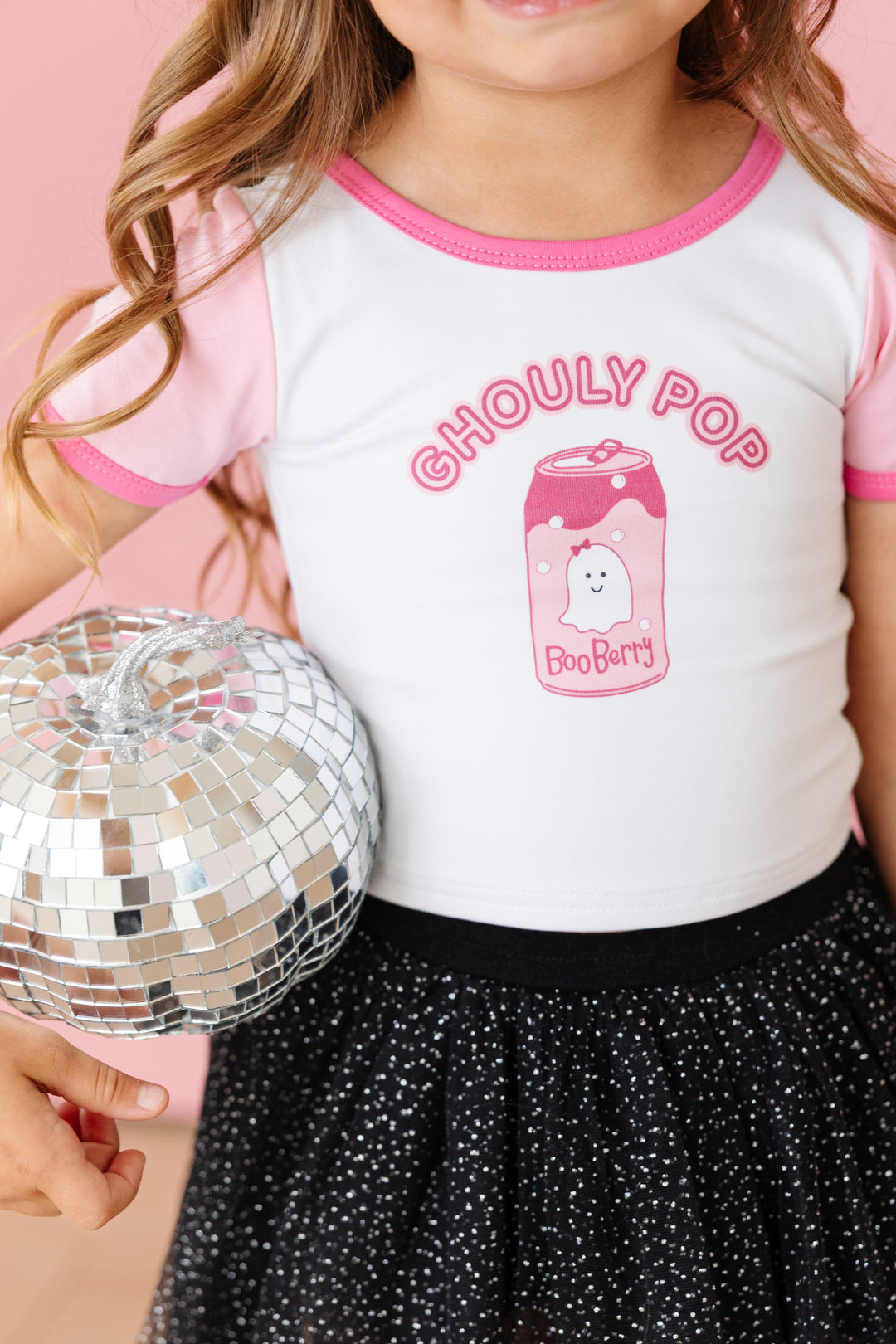 little girl holding mirrored pumpkin in white cotton blend tee with "Ghouly Pop" print and ghost soda can with pink short sleeves and dark pink binding paired with black sparkle tutu skort