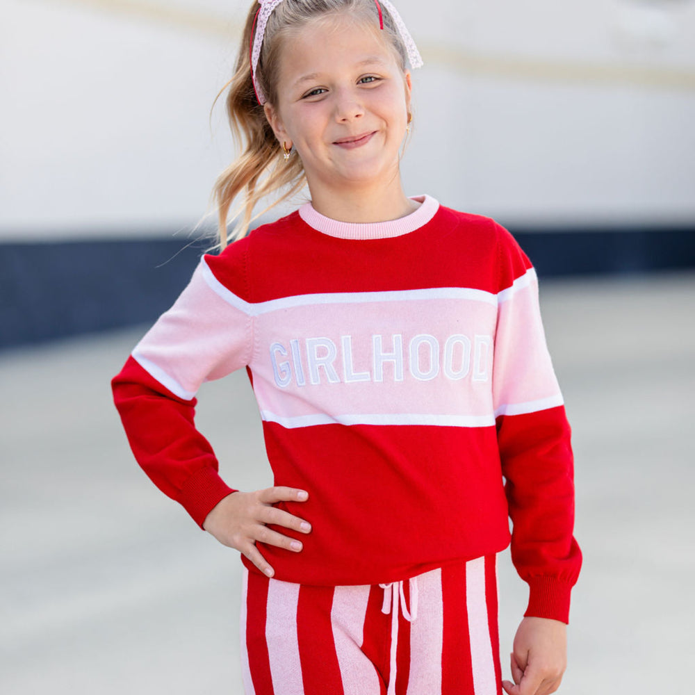 girl in red and pink cotton knit pullover sweater with white embroidered Girlhood patches 