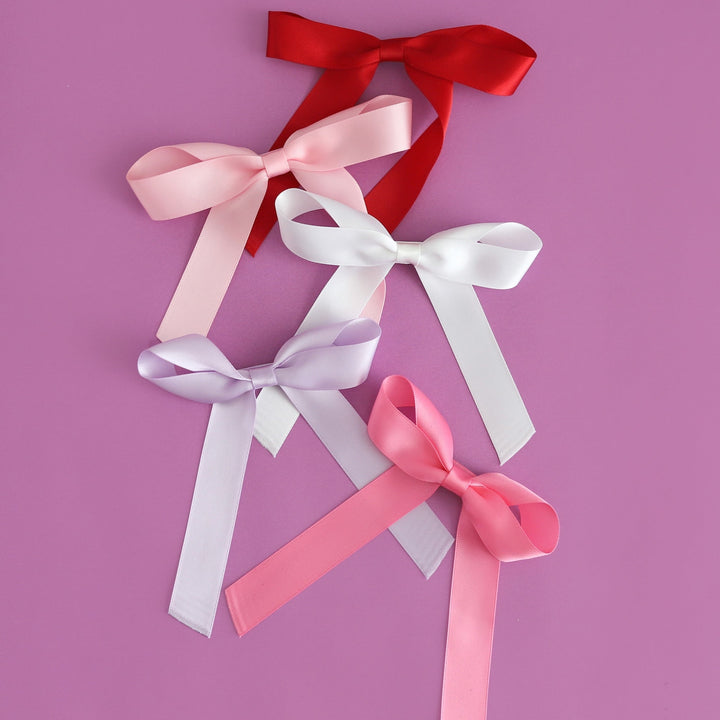 flatlay of five satin ribbon bows on alligator clips for spring and valentines day in red, light pink, white, lavender and hot pink
