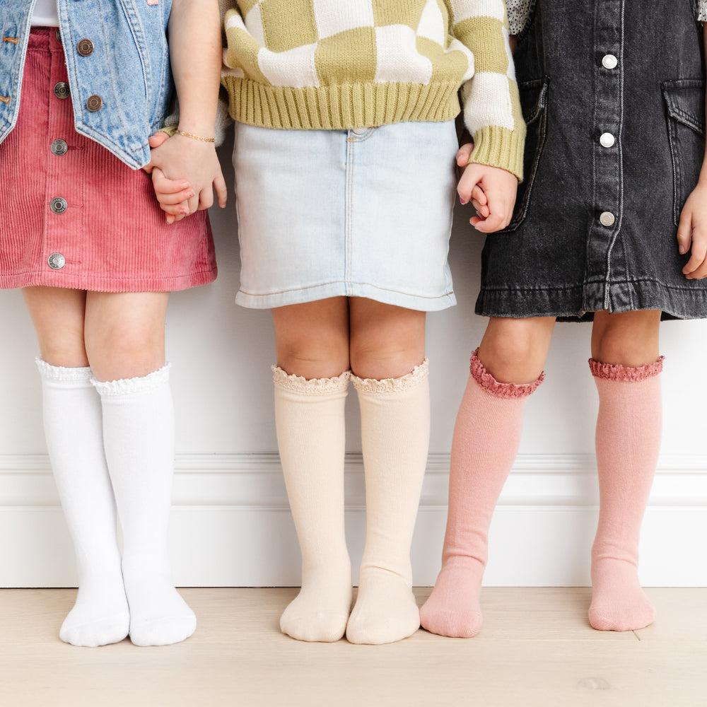 3 girls standing and holding hands wearing neutral set of vintage lace top knee high socks in white, vanilla cream and blush pink
