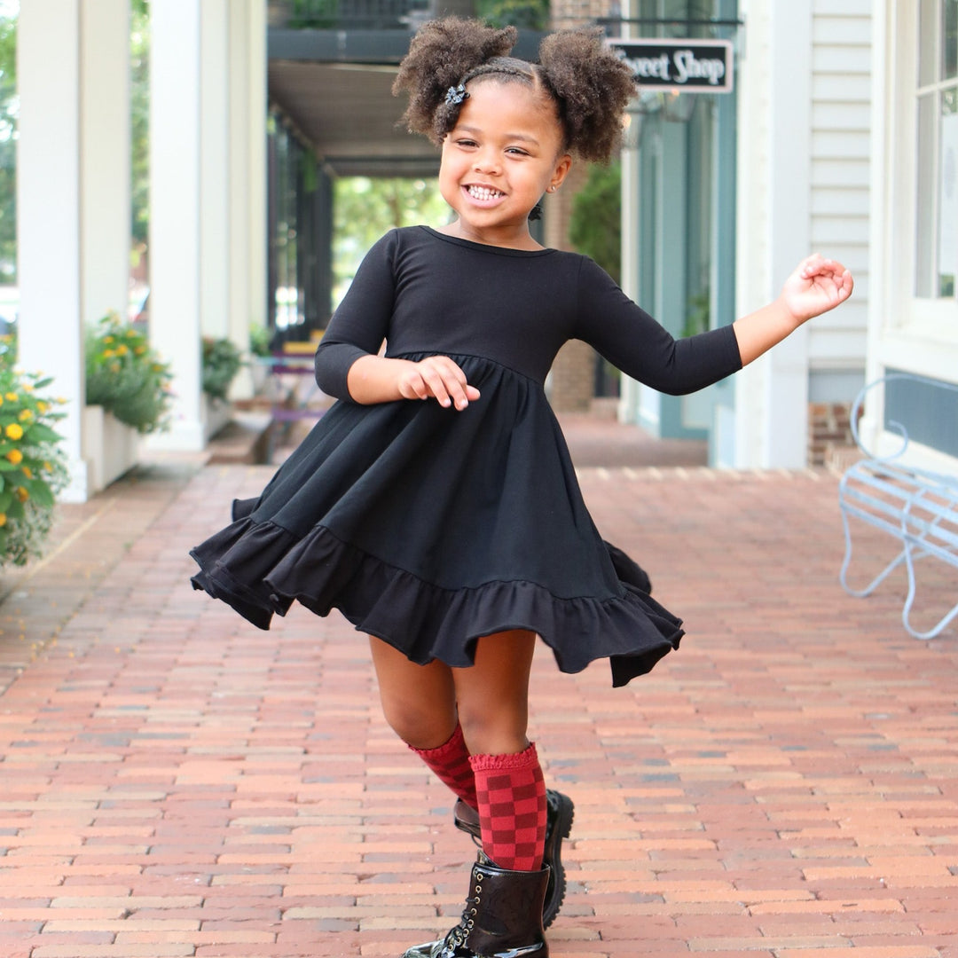 little girl twirling in black long sleeve party dress and red checkered knee high socks