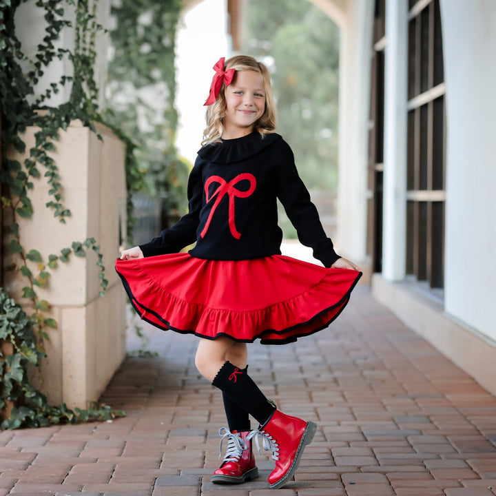 little girl wearing red and black christmas outfit with bow sweater and matching bow knee high socks