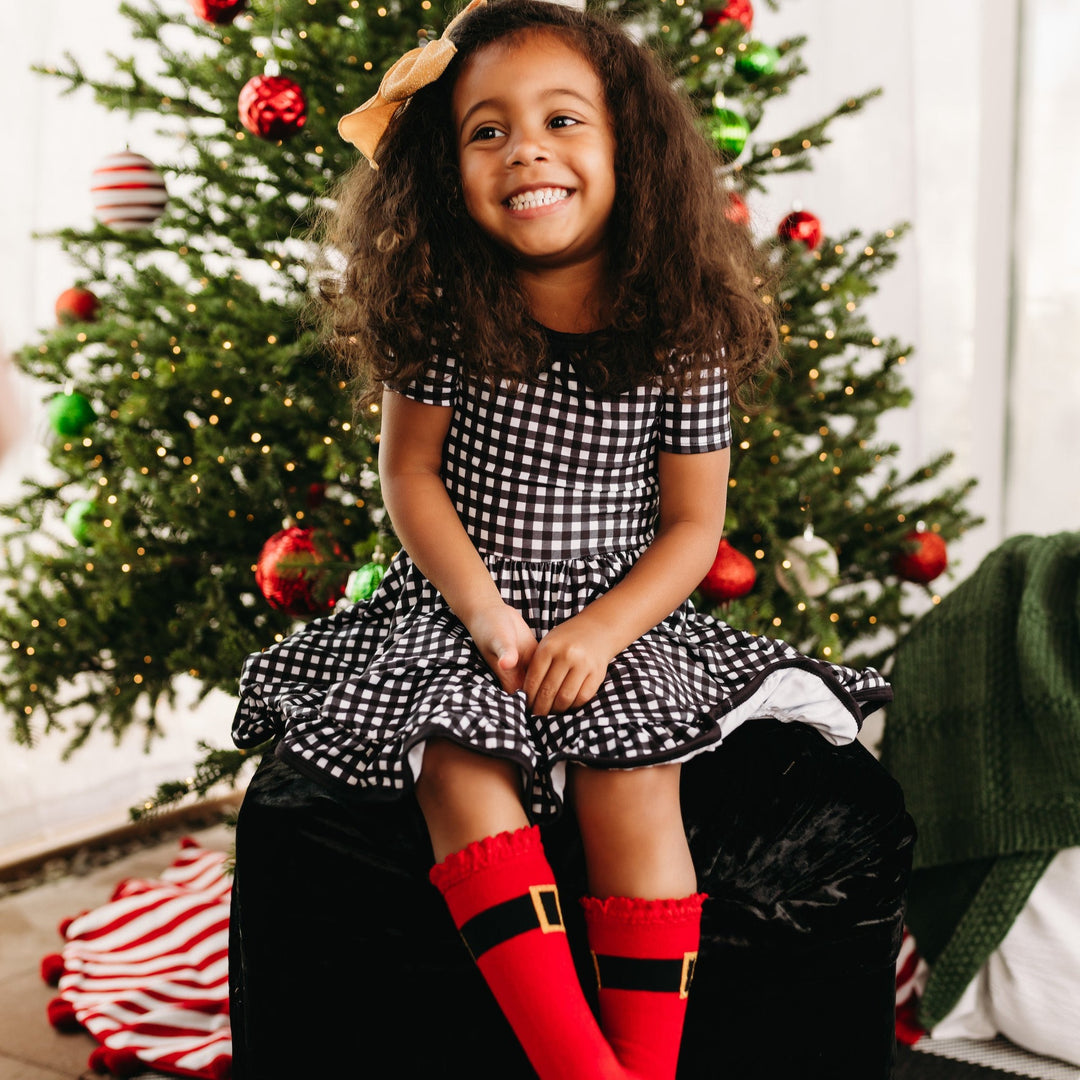 little girl in cute christmas outfit with buffalo plaid twirl dress and santa buckle knee high socks
