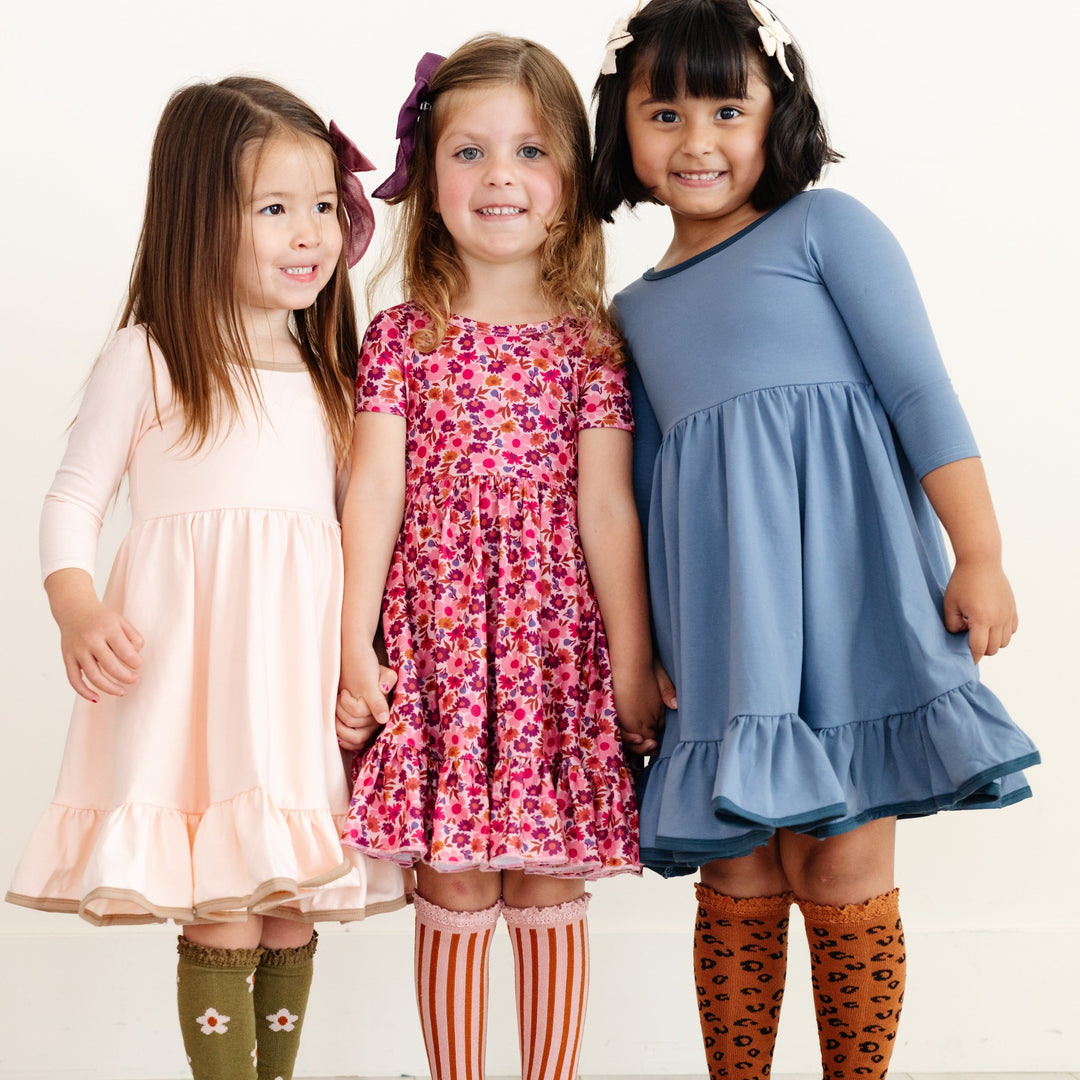 three little girls wearing fall twirl dresses in cream, pink floral and denim blue.