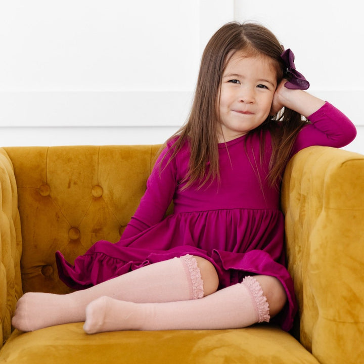 little girl wearing ballet pink knee high socks with magenta twirl dress sitting on a yellow chair