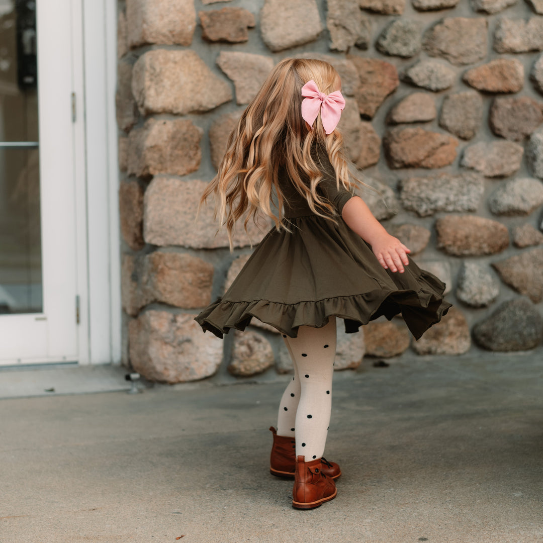girl twirling in olive dress with polka dot tights