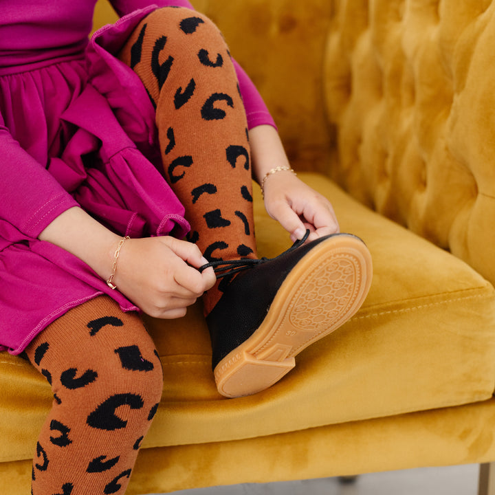 little girl tying shoes in magenta pink dress and leopard print tights